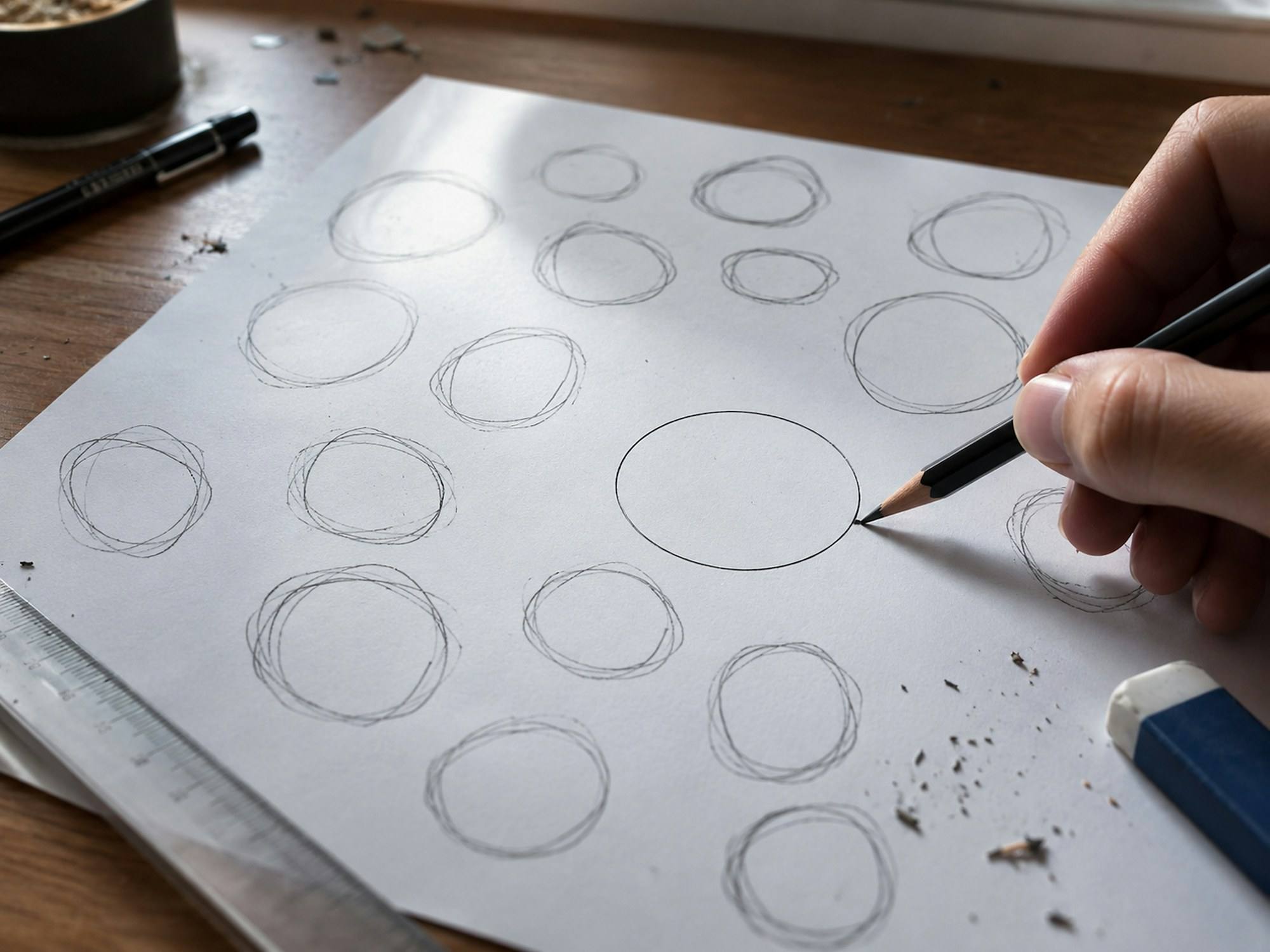 A hand drawing circles in pencil on a sheet of paper